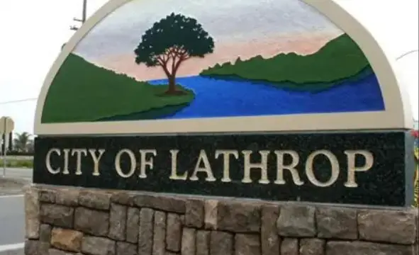 City of Lathrop entrance sign with a semicircular mural of a tree by a river and green hills on a stone base.