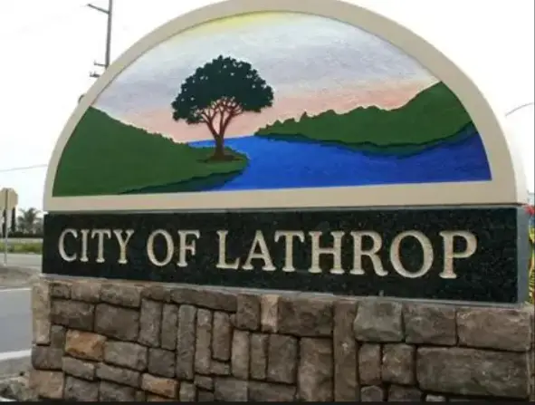 City of Lathrop entrance sign with a semicircular mural of a tree by a river and green hills on a stone base.
