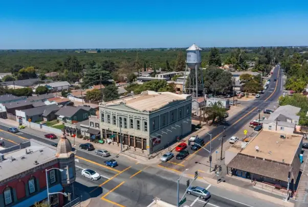 Aerial view of a small-town intersection; a green historic building sits on the corner with storefronts and a tall water tower nearby.